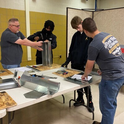 Three students working with their teacher to build with metal