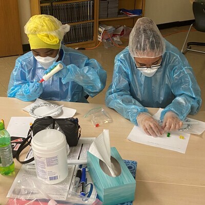 Two students wearing PPE building models with glue and paper