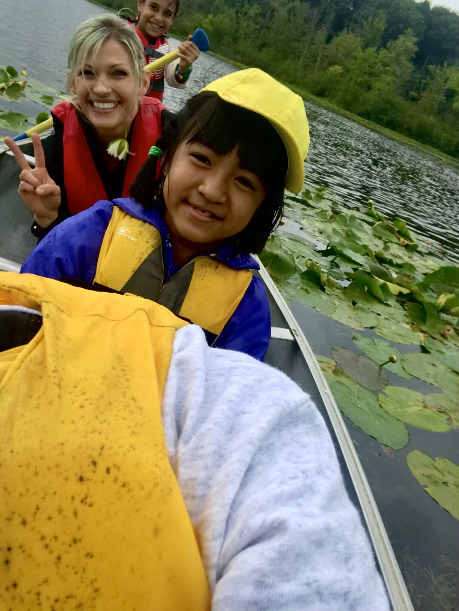 Two students and a teacher smiling in a canoe on a lake