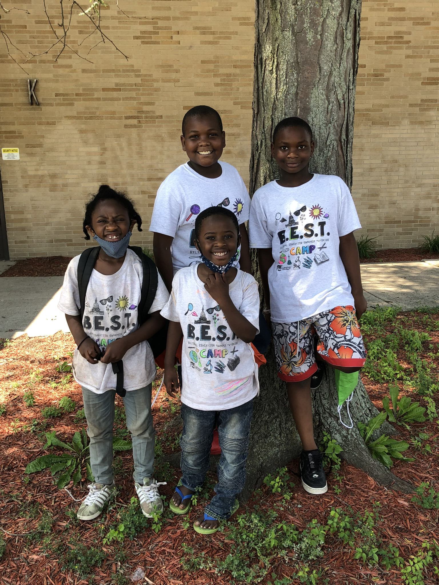 Four students standing under a tree smiling and wearing BEST Camp shirts