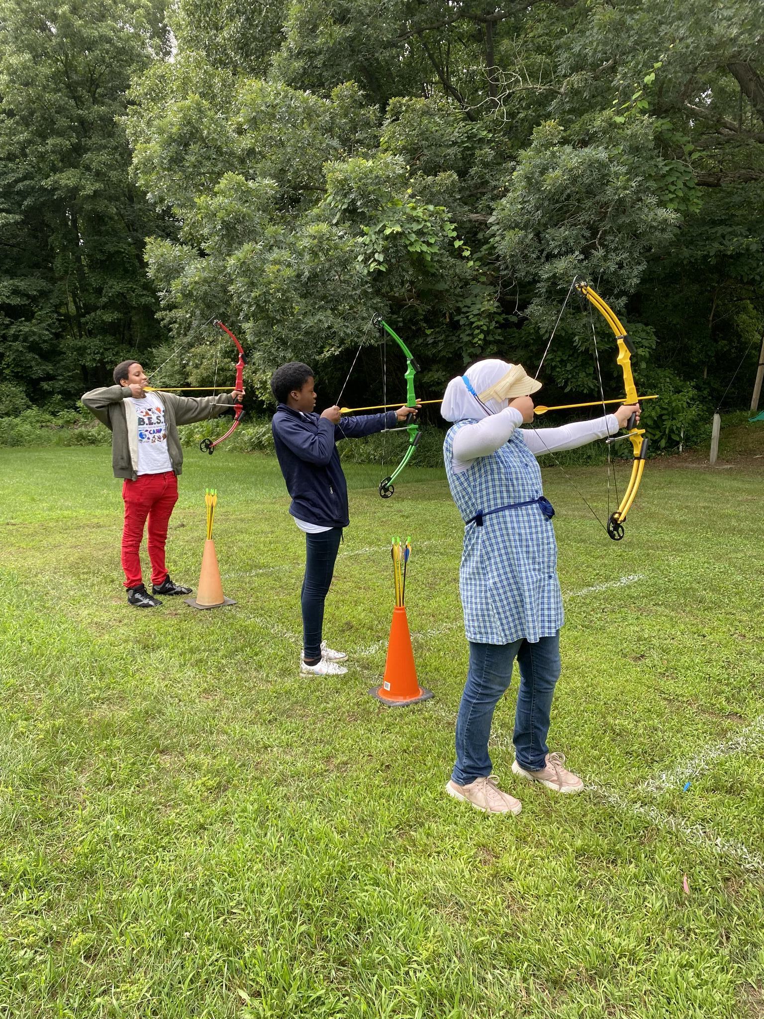 Three students standing ready to shoot an arrow at an outdoor archery range